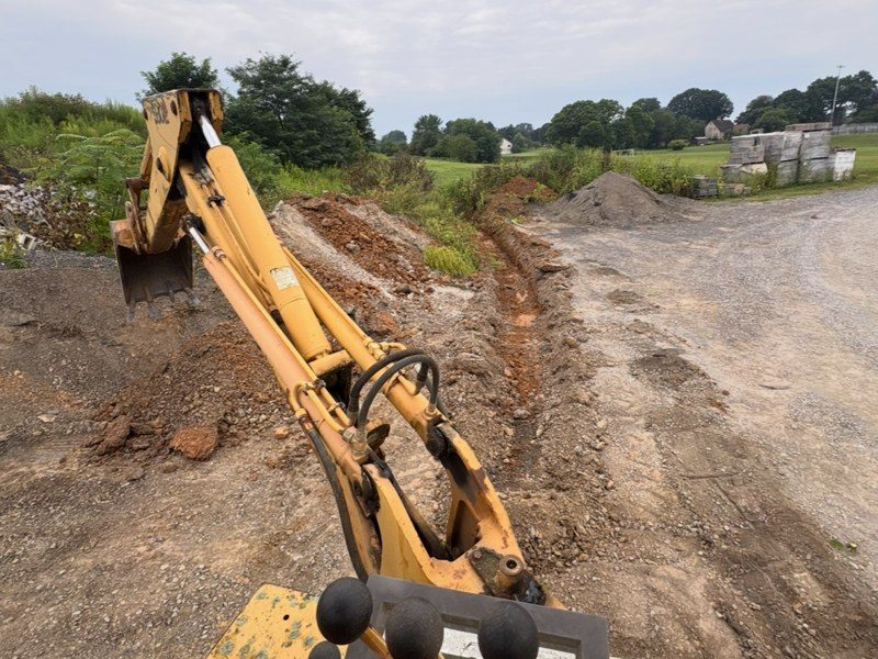 Backhoe cutting a narrow trench on a rural site